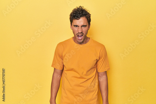Wallpaper Mural Young Latino man posing on yellow background shouting very angry, rage concept, frustrated. Torontodigital.ca