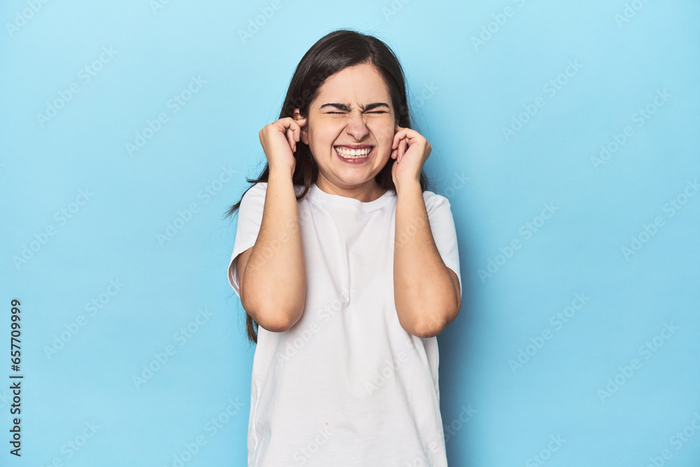 Young Caucasian woman on blue backdrop covering ears with hands. Young Caucasian woman on blue backdrop covering ears with hands.