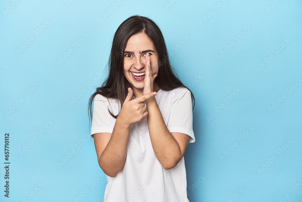 Young Caucasian woman on blue backdrop saying a gossip, pointing to side reporting something. Young Caucasian woman on blue backdrop saying a gossip, pointing to side reporting something.