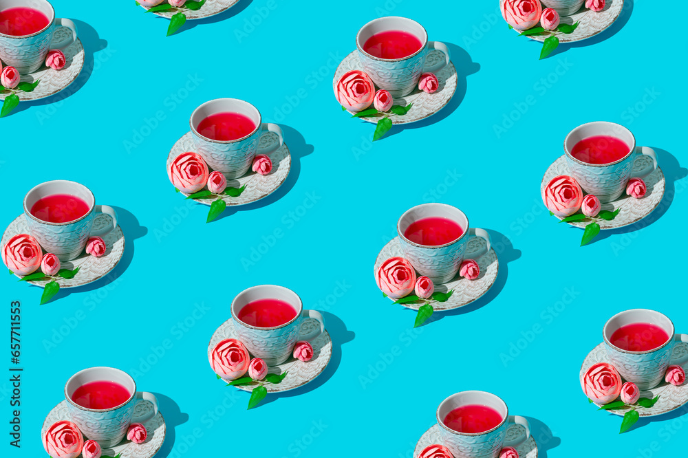 Creative trendy pattern made of cup of tea decorated with pink flowers and green leaves on bright light blue background. Minimal hot drink and flowers concept. Fancy floral tea composition. Creative trendy pattern made of cup of tea decorated with pink flowers and green leaves on bright light blue background. Minimal hot drink and flowers concept. Fancy floral tea composition.