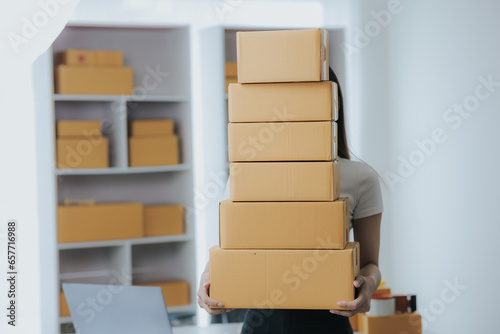 Portrait of a happy Asian woman Starting a small business, SME owner, female entrepreneur Work on receipt boxes and review online orders to prepare boxes for sale to customers. SME online business ide © Witoon