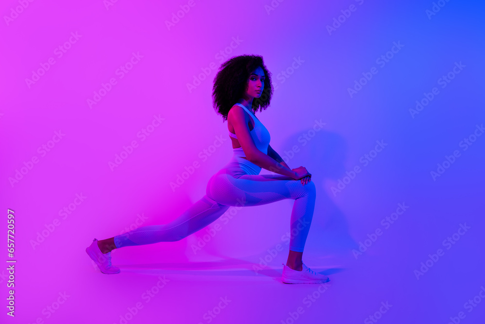 Full size profile portrait of great shape self improvement coach stretching legs isolated on ultraviolet color neon background Full size profile portrait of great shape self improvement coach stretching legs isolated on ultraviolet color neon background