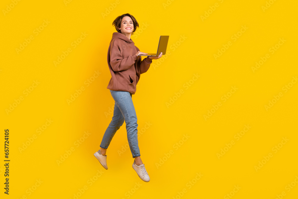 Full size body photo of jumping programmer girl using netbook working remote no limits freelance job isolated on yellow color background Full size body photo of jumping programmer girl using netbook working remote no limits freelance job isolated on yellow color background