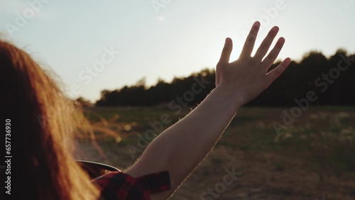 Fototapeta Naklejka Na Ścianę i Meble -  Woman leans out of window and holds hand riding car across rural site at sunset