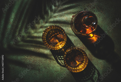 Whiskey, scotch or bourbon in glasses and bottle, green stone background with hard light, shadows and sun glare, copy space