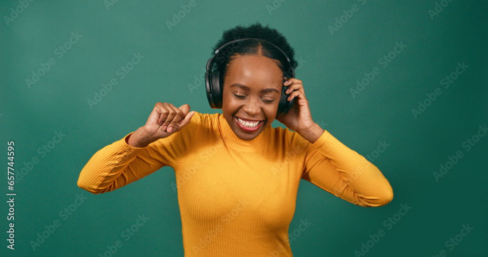 Wide shot, young Black woman dancing with headphones, green studio background