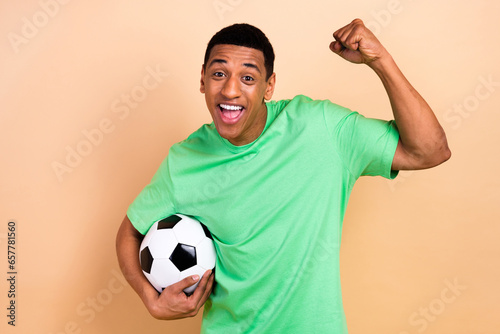 Photo portrait of nice young guy raise fist winner football playing dressed stylish green garment isolated on beige color background
