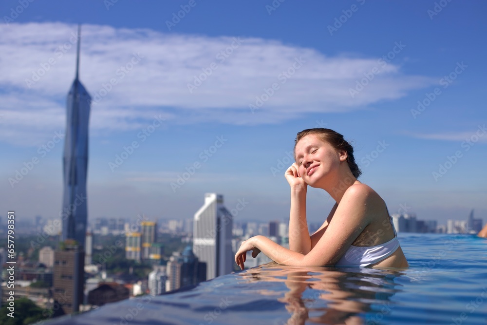 Portrait of happy young woman in swimming pool on the rooftop of skyscraper hotel with beautiful city urban view Portrait of happy young woman in swimming pool on the rooftop of skyscraper hotel with beautiful city urban view