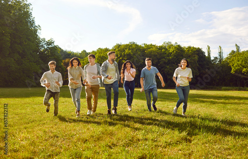 Group of several happy, cheerful friends having fun on a sunny summer day in nature. Seven happy young people running together on a green grass lawn in the park