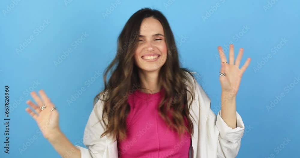 Woman in pink top, white shirt dancing, showing victory, v sign. Funny unusual brunette woman hair having fun, hands up, grimaces, smiling, dancing in studio against blue background. Music, dance. Woman in pink top, white shirt dancing, showing victory, v sign. Funny unusual brunette woman hair having fun, hands up, grimaces, smiling, dancing in studio against blue background. Music, dance.