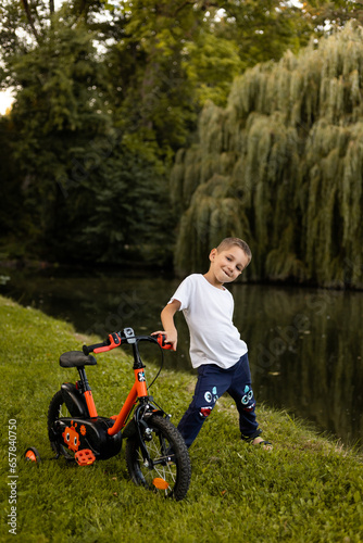 A boy rides a bicycle in a park near the lake. Schoolboy's day off