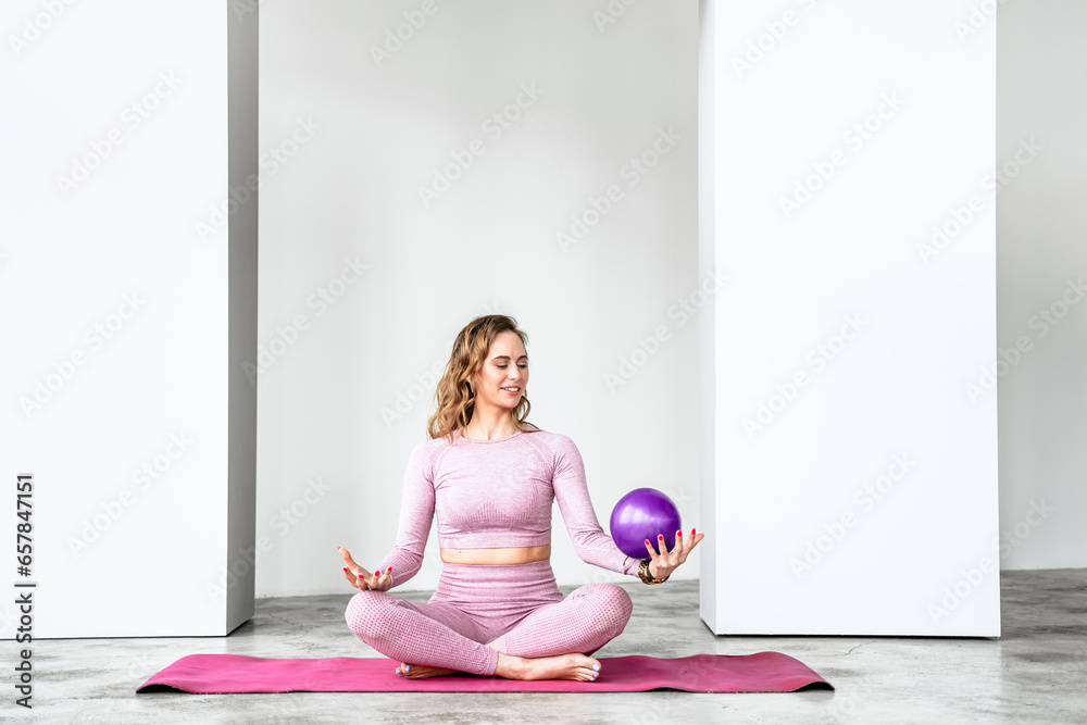 Slim woman with rubber ball rubber ball for rhythmic gymnastics. Training yoga in pink tight-fitting tracksuit in fitness gym. Stretching, pilates practice. Workout, exercises at home on fitness mat