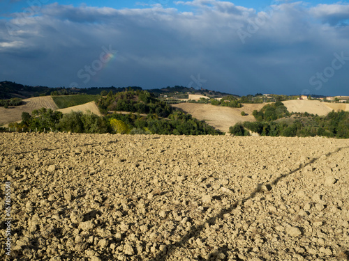 Scenic view of tilled soil with rolling hills, trees and a partial rainbow in a dark sky on a sunny day in San Procolo, Monte Vidon Combatte in the Marche Region; Province of Fermo, Italy photo