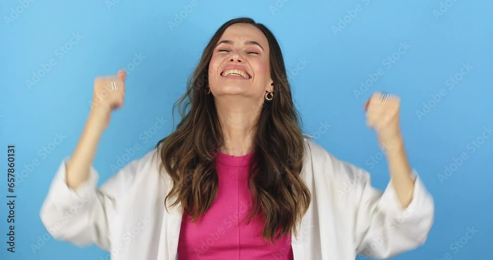 Brunette curly woman wear pink top and white shirt, pointing finger camera on you doing winner gesture celebrating clenching fists yes, make win gesture isolated on blue background. Brunette curly woman wear pink top and white shirt, pointing finger camera on you doing winner gesture celebrating clenching fists yes, make win gesture isolated on blue background.