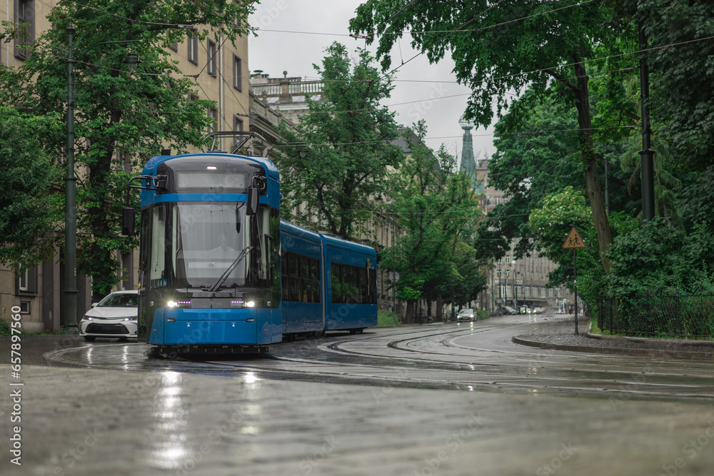 Blue polish tram in the middle of Krakow city on a rainy day. Beautiful picture of a tram, public service transport during a light drizzle rain