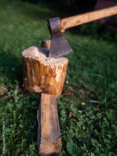 Old rusty metal axe with wooden handle on a fire wood cutting block on green grass. Old style equipment.