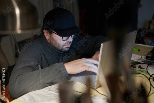 A close-up shot of a man using a laptop in a dimly lit room, engrossed in his digital work during the late hours of the night