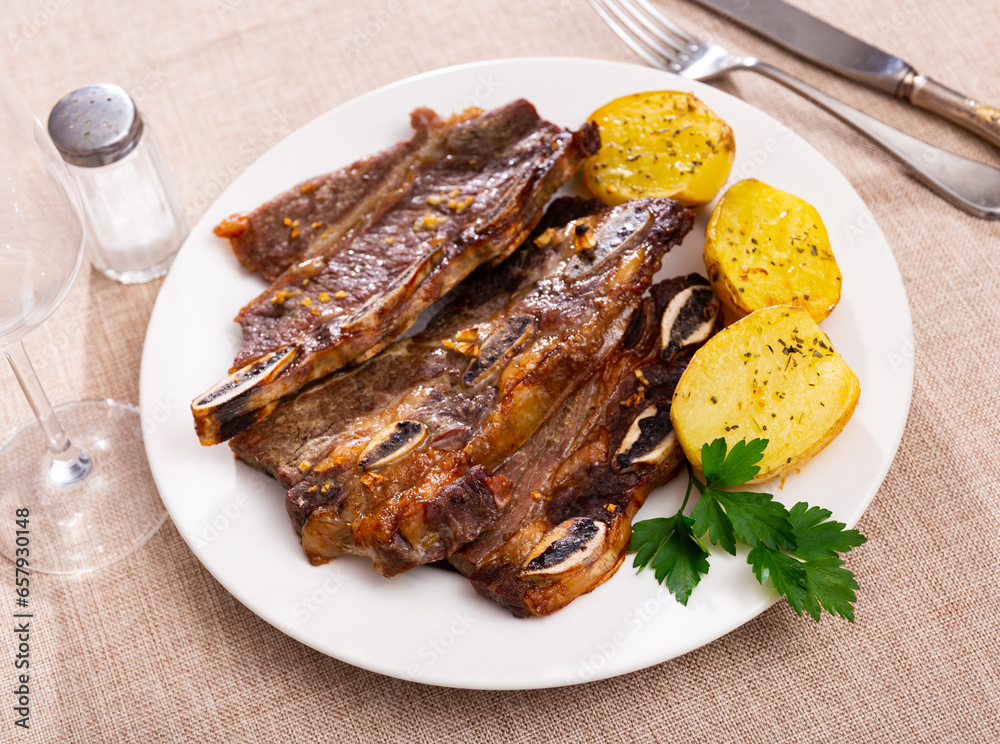 Fried steak of ribs and potato pieces dished up in a plate on the laid restaurant table