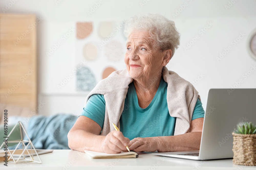 Senior woman with laptop writing in notebook at home Senior woman with laptop writing in notebook at home