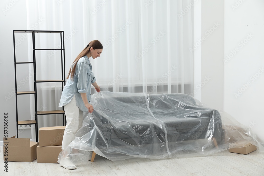 Young woman putting plastic film away from sofa at home - obrazy, fototapety, plakaty 