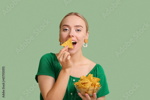 Pretty young woman eating nachos on green background