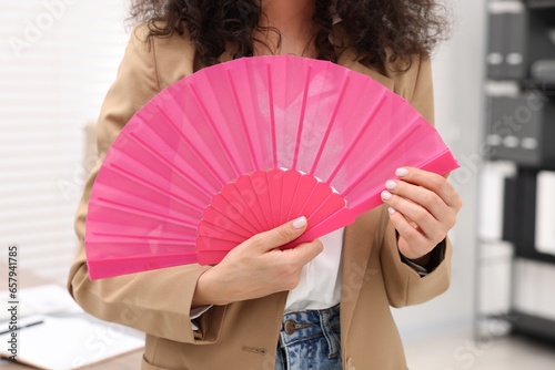 Woman with pink hand fan in office, closeup