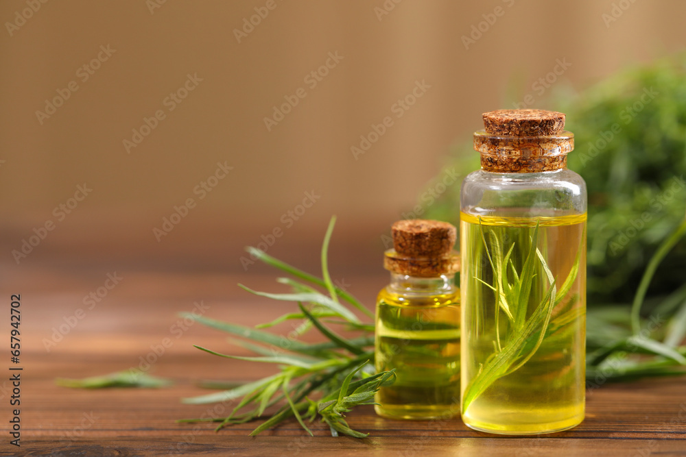 Bottles of essential oil and fresh tarragon leaves on wooden table. Space for text Bottles of essential oil and fresh tarragon leaves on wooden table. Space for text