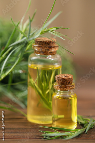 Bottles of essential oil and fresh tarragon leaves on wooden table