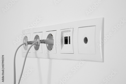 Foto Many power sockets with plugs, ethernet and TV coax plates on white wall indoors