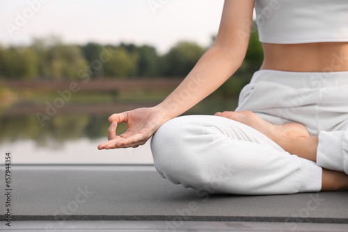 Woman practicing Padmasana on yoga mat outdoors, closeup and space for text. Lotus pose