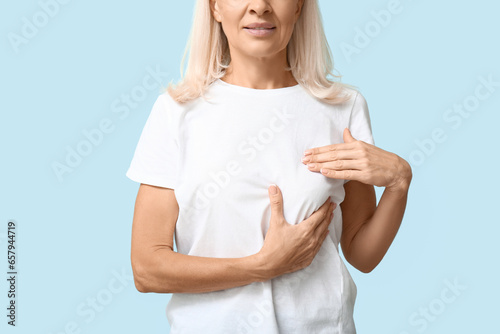 Mature woman checking her breast on blue background. Cancer awareness concept photo