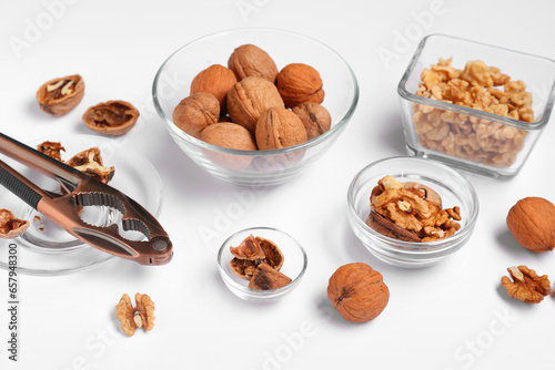 Bowls with walnuts and nutcracker on white background