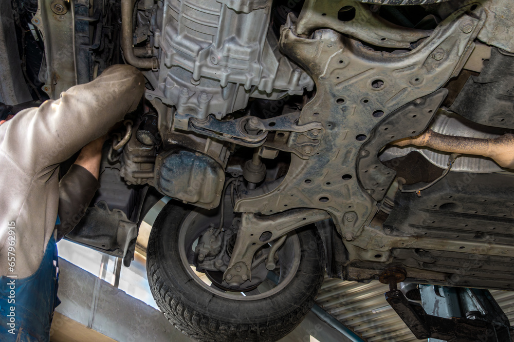 An auto mechanic maintains a car on a service station lift