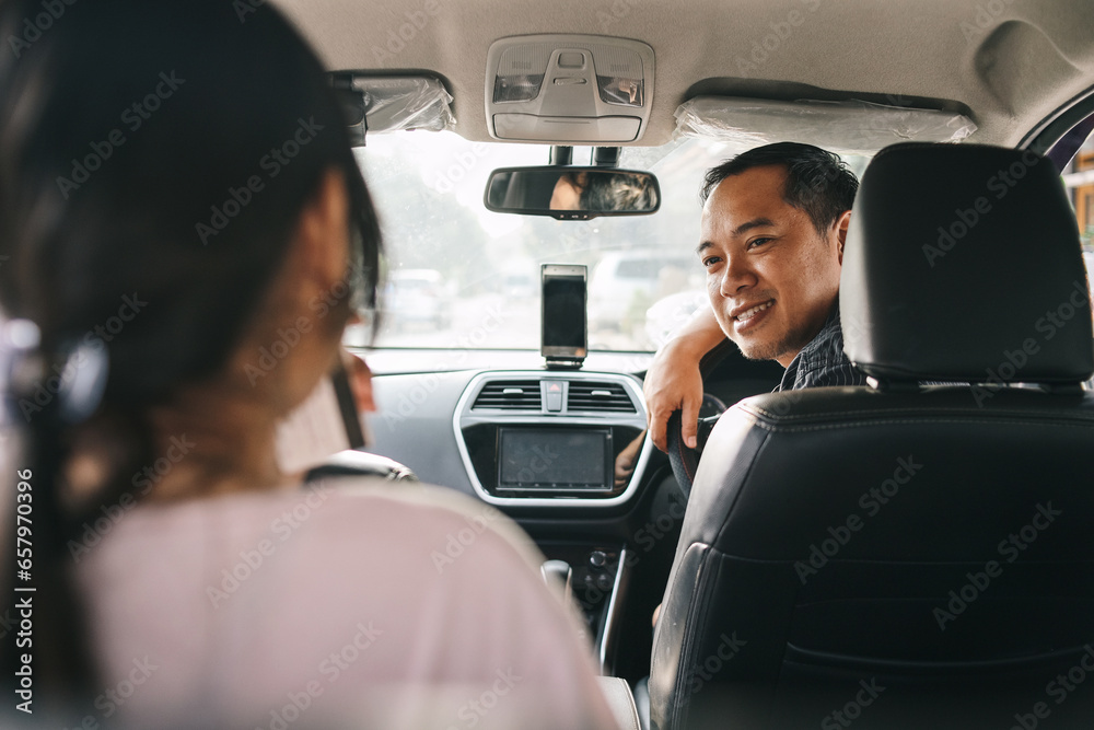Online taxi driver smiling while turning over to the backseat looking and talking with clients