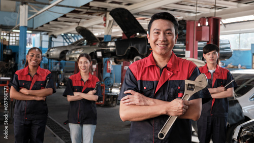 Portrait of professional workers team, male Asian supervisor arms crossed with fixing tools in front of mechanic colleagues, guarantee car repair jobs success with cheerful smiles at service garage.