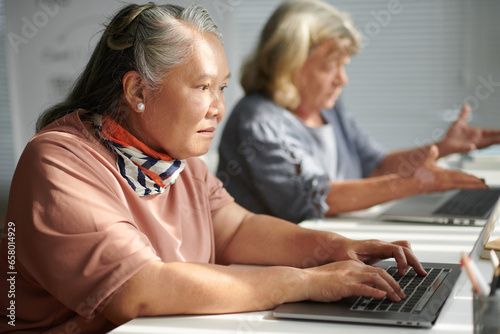 Elderly woman working on laptop in class for seniors © DragonImages
