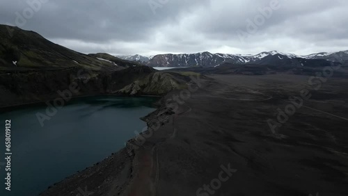 Hnausapollur aerial view in the highlands of Iceland, with a mountain covered in snow in the background, different shades of grey and green, and a blue crater laker in a beautiful landscape. photo