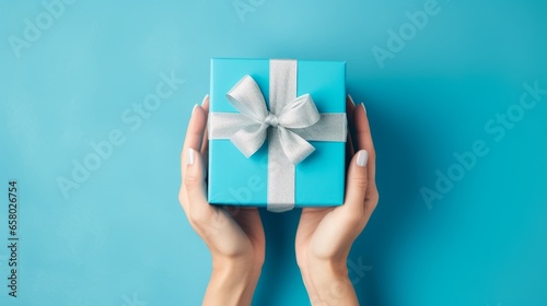 Generative AI Flat lay composition for happy birthday party. Minimalistic greeting card. Women's hands hold a blue gift box with a satin bow on a blue background. Top view.