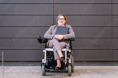 smiling business woman using a electric wheelchair holding a folder looking at camera, concept of entrepreneurship and diversity, copy space for text