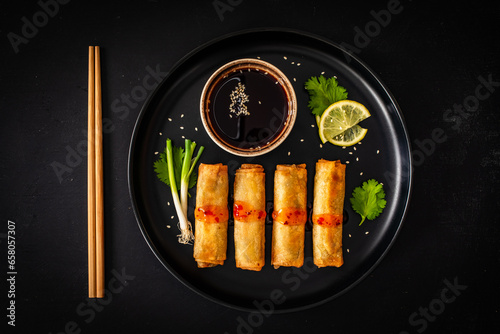 Foto Vegetable filled spring rolls and soy sauce on black wooden table