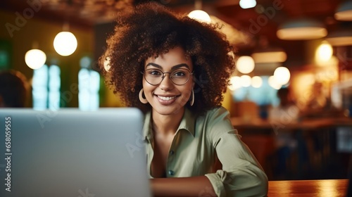 portrait of young curly haired woman smiling at her laptop in a cafe