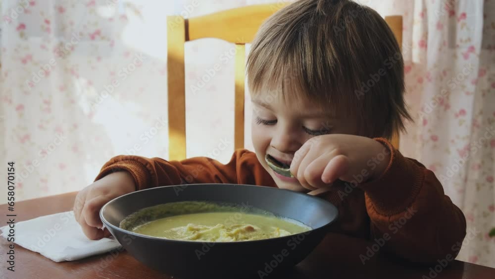 Preschooler boy eating cream soup sitting at table in kitchen. Kid having lunch at home. Preschooler boy eating cream soup sitting at table in kitchen. Kid having lunch at home.