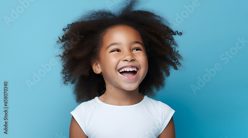 Close-up of a smiling African American little girl with white perfect teeth, isolated on a blue studio background with copy space. Children's Dental Care. Dentistry concept. photo