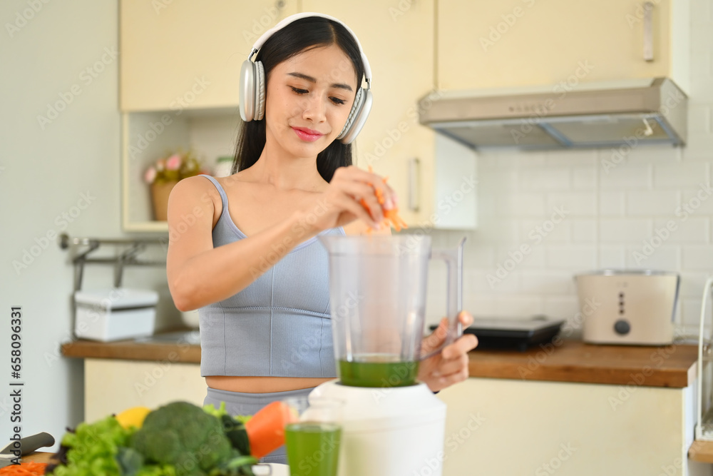 Happy young woman making healthy green smoothie with blender in kitchen. Healthy lifestyle concept