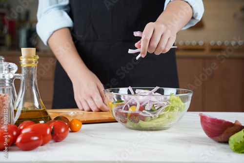 The Girl adds red onions to salad of fresh vegetables. The Girl in the process of making vegetable salad.