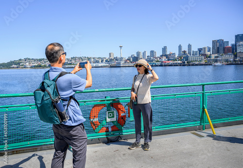 Tourists taking photos using smartphone on the ferry at Elliott Bay. Seattle skyline and the historic Space Needle in the background. Seattle. Washington State.