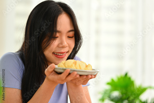 Pretty young asian woman eating pastry with great pleasure while spending weekend time at home
