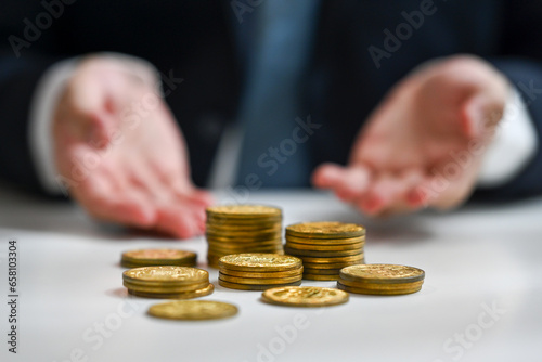 Stack of gold coins on white table with businessman sitting in background. Finance, investment and save money concept