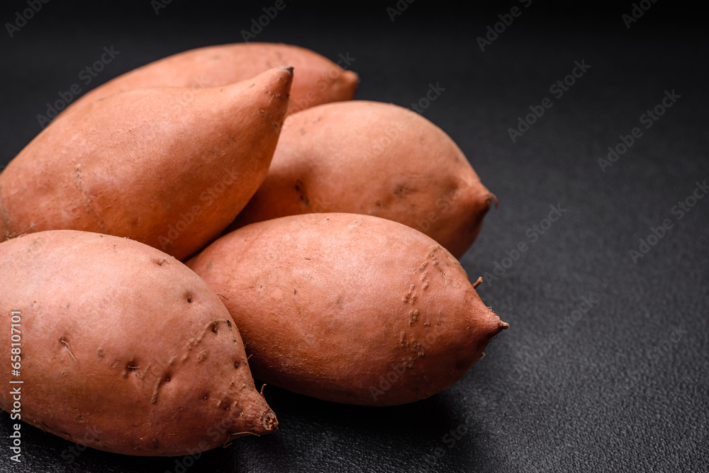 Fresh large pink sweet potato tubers with tomatoes and spices on a dark background Fresh large pink sweet potato tubers with tomatoes and spices on a dark background