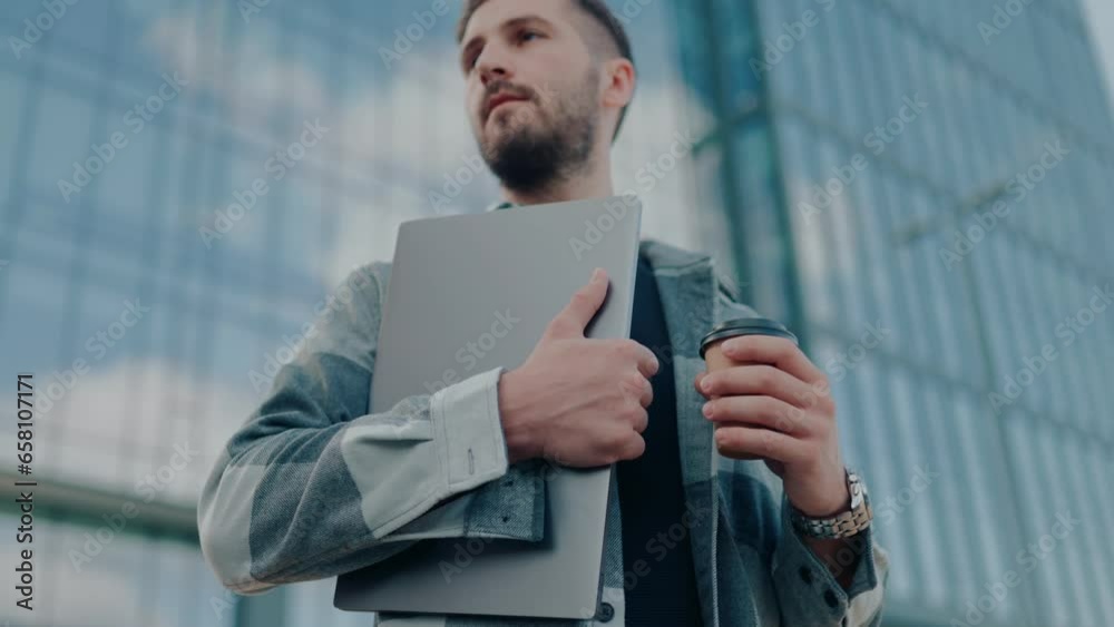 In this striking image, a young male worker or student proudly holds his laptop against the backdrop of a dynamic city street and tall buildings. In this striking image, a young male worker or student proudly holds his laptop against the backdrop of a dynamic city street and tall buildings.